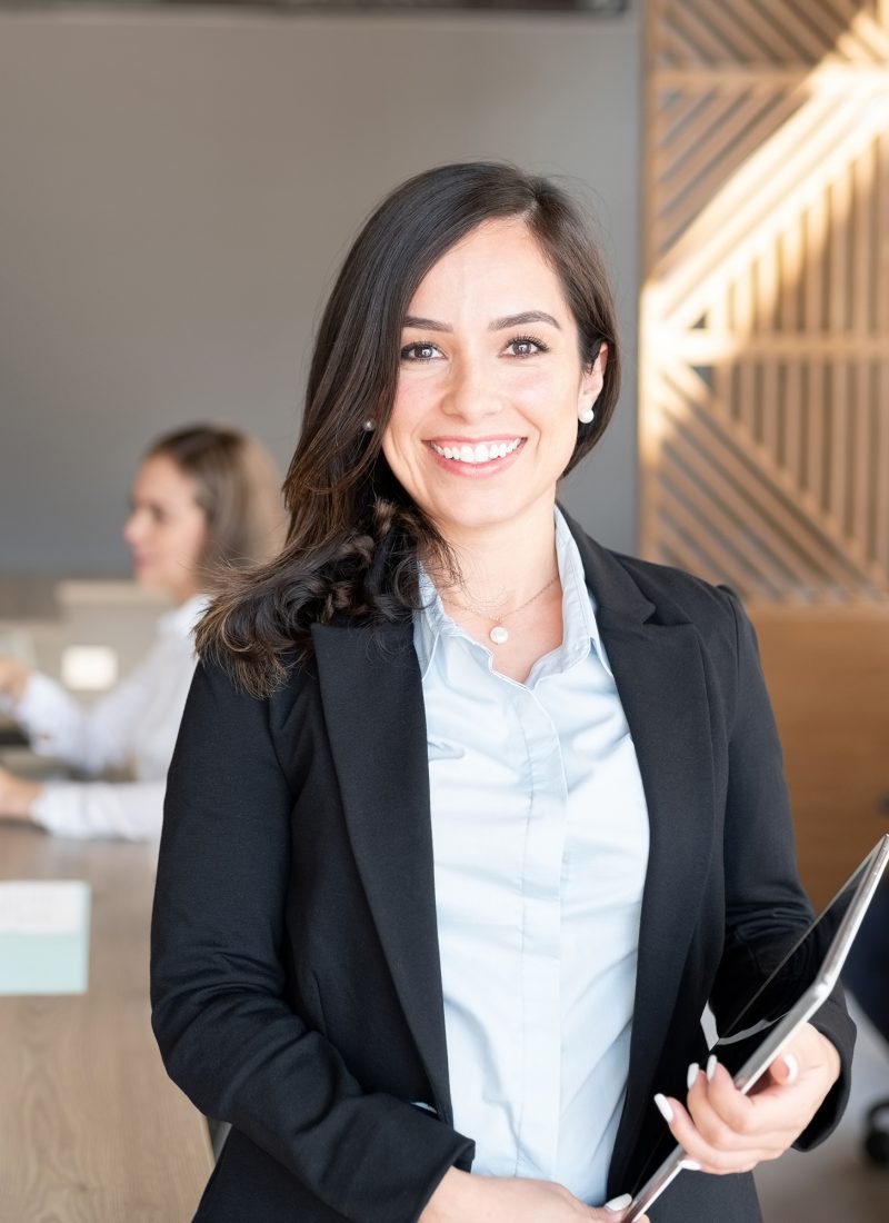 Portrait of female lawyer holding digital tablet standing in office with colleagues working in background